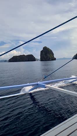 Vídeo-Vertical,-Barco-Tradicional-Filipino-Bangka-Navegando-Entre-Islas-Y-Rocas-Pintorescas,-Cámara-Lenta