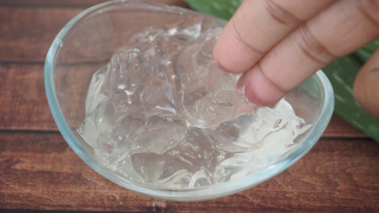 Close-up of hand touching aloe vera gel in a glass bowl