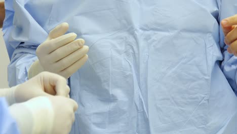 close-up of a surgeon's hands as another doctor helps to put on sterile gloves in operation for surgery