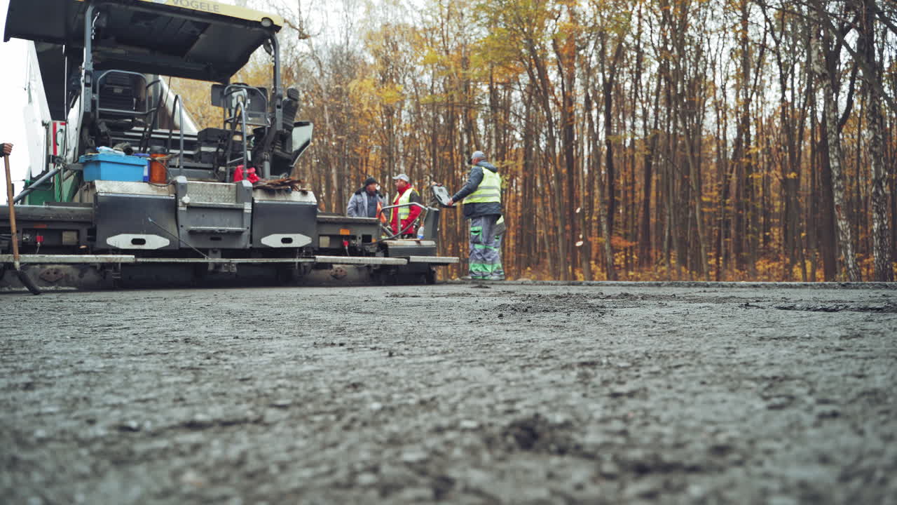 Roadworks repaving process. Workers applying new hot asphalt using road construction machinery and power industrial tools. Camera moves forward.