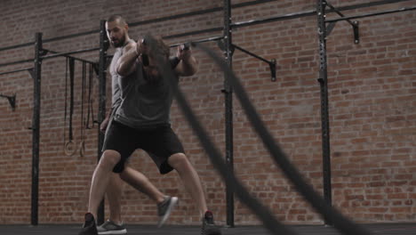 coach watching sportsman exercising with battle ropes
