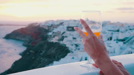 wine glass with an orange wine in front of oia village, santorini