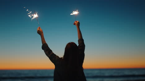 woman playing with sparklers on beach at sunset enjoying new years eve celebration girl celebrating independence day waving sparkler firework by the sea