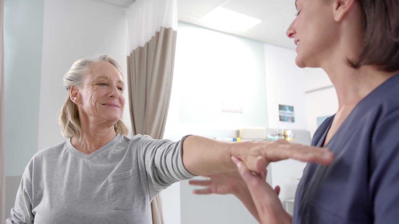 백인 여성 물리치료사가 재활 센터에서 여성 노인 환자의 손을  ⁇ 고 있습니다.