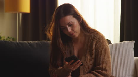 shocked woman sitting on sofa at home using mobile phone to check social media message and scrolling online 1