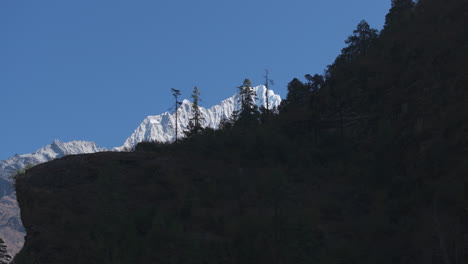 Drone-captures-snow-capped-mountain-behind-trees-on-a-hill-near-Everest-Base-Camp,-Nepal