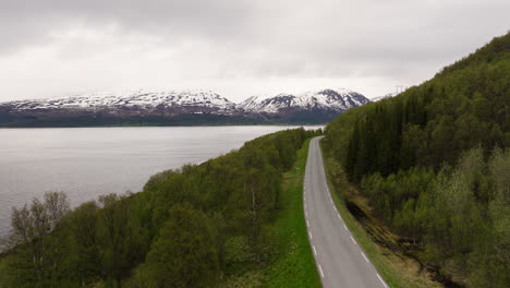 landscape of unwinding road overlooking the sea and alps in distance on a cloudy day in northern norway