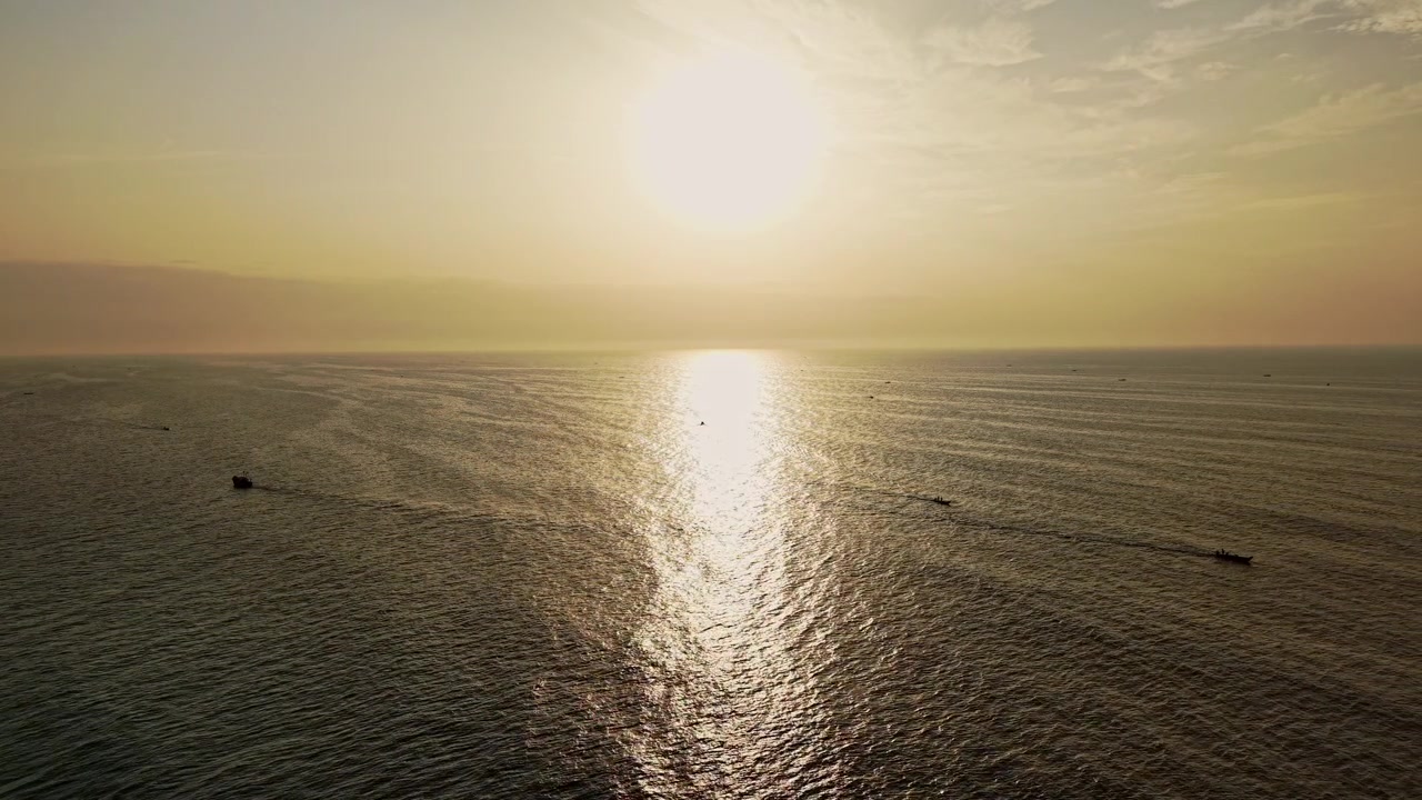 Aerial drone view of sunrise over Bay of Bengal with fishing boats on calm sea near Chennai coastline creating golden reflections and peaceful morning scenery