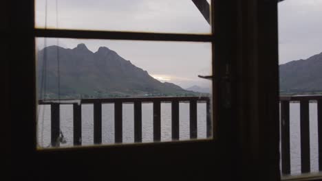 a view of a lake and mountains during sunset on a cloudy day seen from log cabin window
