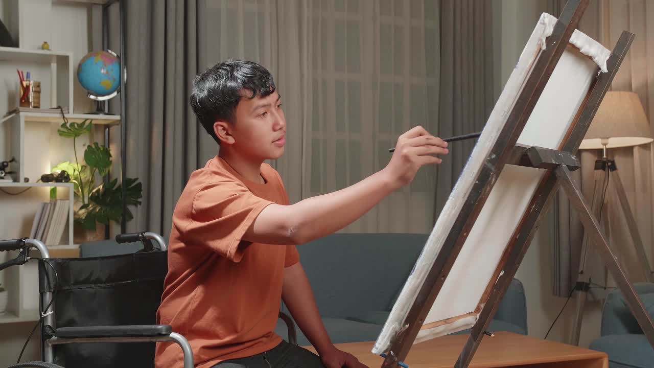 Happy Asian Artist Boy In Wheelchair Holding Paintbrush Mixed Colour And Thinking Before Painting On The Canvas