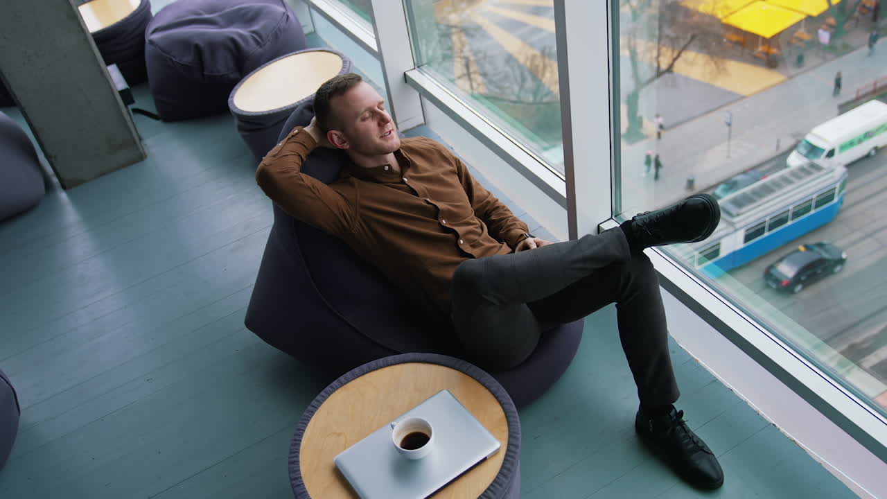 Businessman relaxing in office. Young man sitting in comfortable armchair with closed eyes and dreaming at daytime next to the window with city view. Top view.