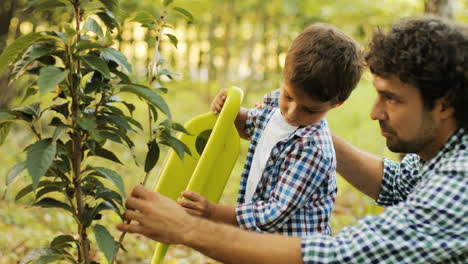 Portrait-of-a-boy-and-his-dad-watering-a-tree.-Dad-helps-his-son.-Happy-family.-Blurred-background