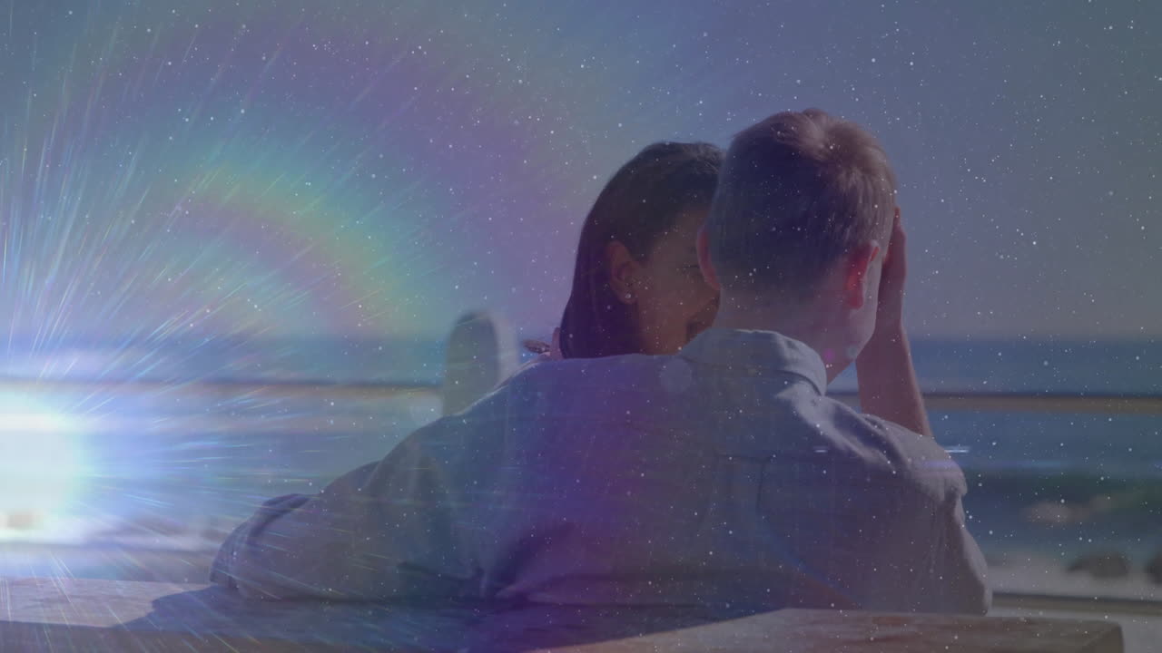 Animation of couple relaxing by ocean with rainbow and starry sky