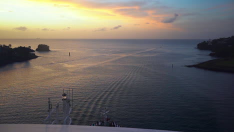 Timelapse-view-from-a-cruise-ship-board-sailing-out-of-a-harbor-in-the-Caribbean-sea,-heading-for-the-wide-open-ocean-towards-a-golden-sunset-on-the-horizon,-avoiding-cliffs-and-reefs,-timelapse-FHD