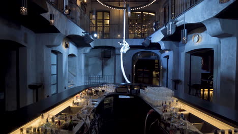 female aerialist spinning on aerial silks hanging above a club bar