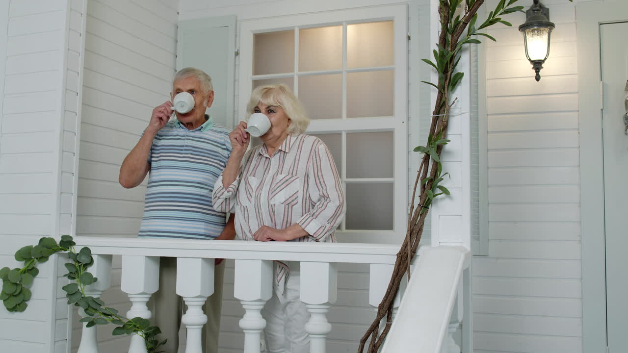 Senior elderly Caucasian couple drinking coffee, looking ahead in porch at home. Mature family