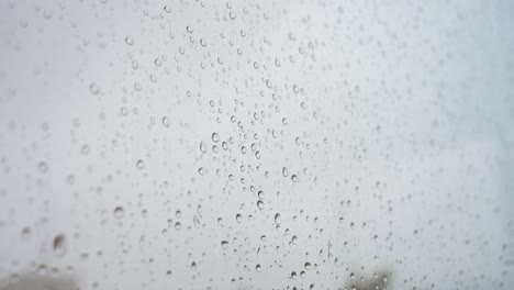 a close-up focus of heavy rain drops is seen through a window glass