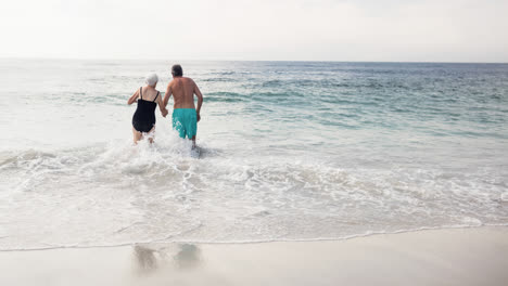 una pareja de ancianos caucásicos de vacaciones se toman de la mano caminando por el mar.