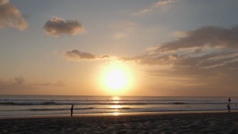 Chico-De-Silueta-En-La-Hermosa-Playa-De-Bali-Al-Atardecer-Pateando-La-Pelota-Con-Olas-Océano-Cielo-Nubes-Arena-Y-Mar