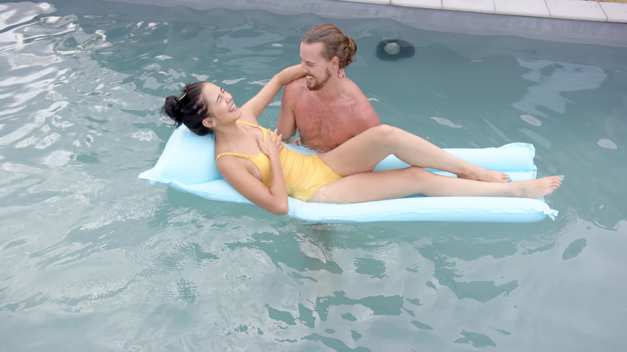 una joven pareja biracial se relaja en un flotador de la piscina