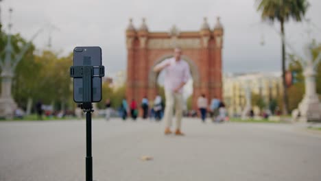 Man blogger making videos using selfie stick phone smartphone taking photo with dance for internet blog on street. Young guy tourist having video call on cellphone walking outdoors in Barcelona spain