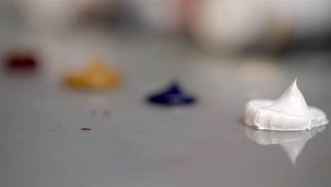 rack focus pulls across blobs of oil paint on silver reflective desk