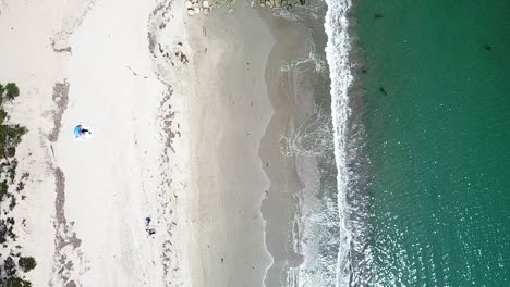 olas turquesas del océano rompiendo en una playa de arena limpia y rocas, california