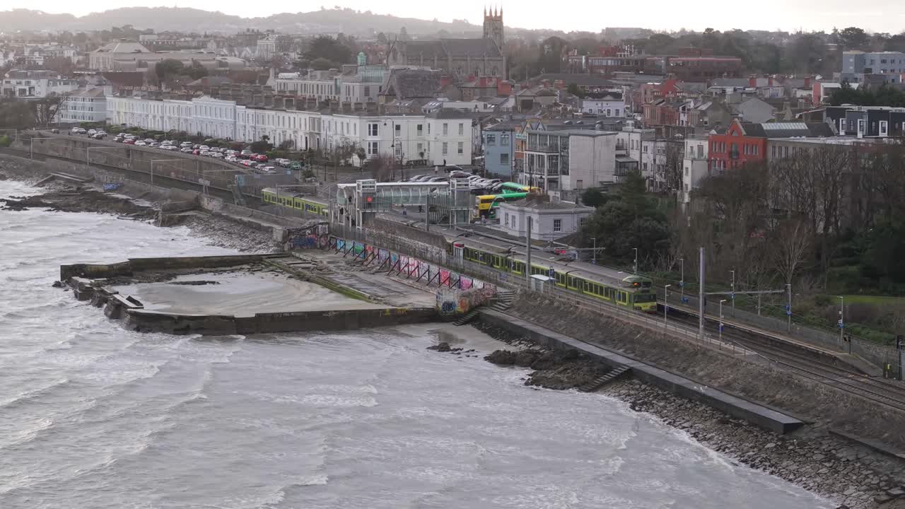Coastal train passing Blackrock Dublin, waves crash near urban seaside town