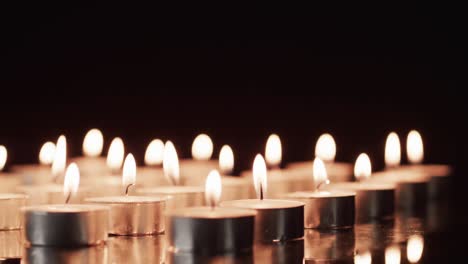 video of rows of tea candles with white flames and copy space on black background