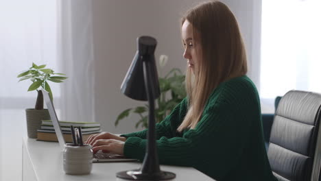 young woman is working alone in big offices at daytime typing text on keyboard of modern laptop with wireless internet connection female office worker