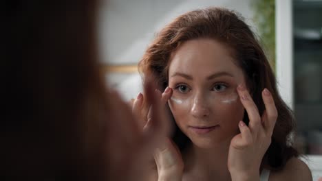 mujer aplicando crema para los ojos en el baño.