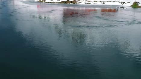 la superficie del agua brilla mientras la nieve todavía yace en la colina