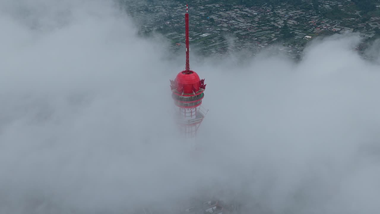 Torre rossa che emerge da dense nuvole con montagne e città