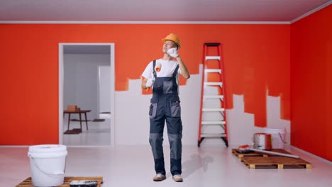 full body of asian man painter wearing safety helmet dancing while standing with painting wall in room
