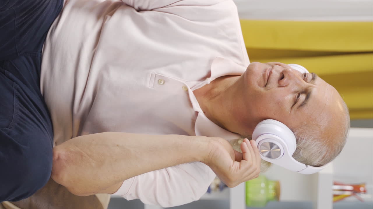 vídeo vertical de un anciano infeliz escuchando música con auriculares.