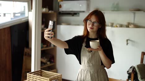 A-red-haired-potter-in-glasses-photographs-her-work-with-her-phone