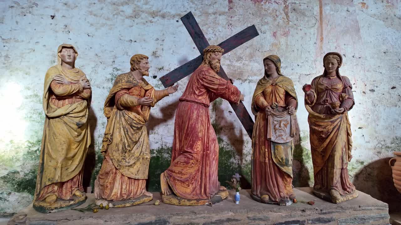 Slow forward shot of painted wooden statues depicting Jesus carrying cross with surrounding figures in private chapel, Mayenne