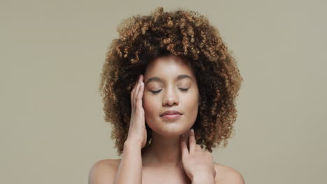biracial woman with dark hair touching face on beige background with copy space, slow motion