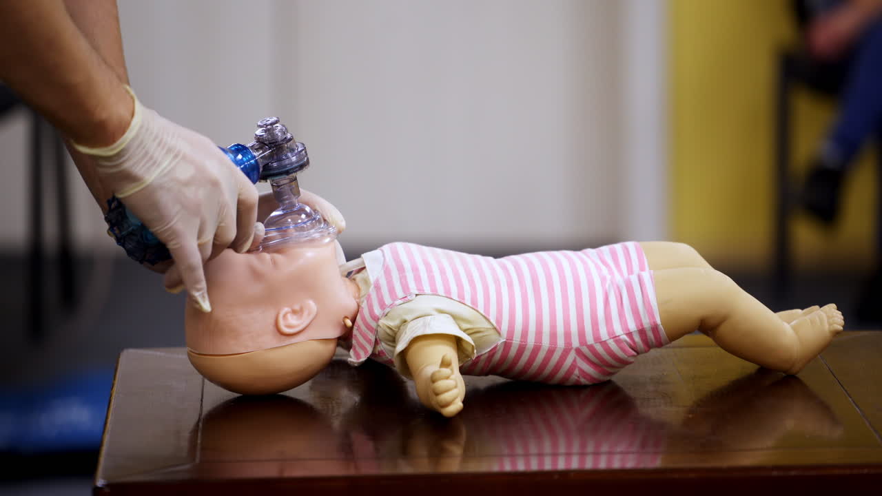 Demonstration of cpr on a baby model. Instructor in medical gloves showing the right breathing exercise on a dummy in training center. Side view.