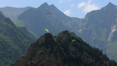 paragliding pilots fly paragliders among clouds and green mountains.