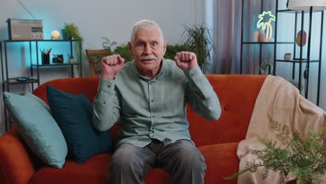 excited senior grandfather man on sofa watching interesting tv serial, sport game online at home