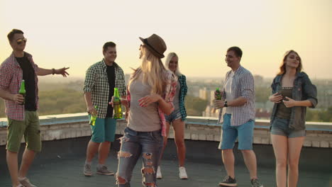 the russian blonde is dansing on the roof with her five friends. she enjoys this time with beer and good mood. she is wearing in fashionable hat ripped jeans white shirt and red plaid t-shirt.