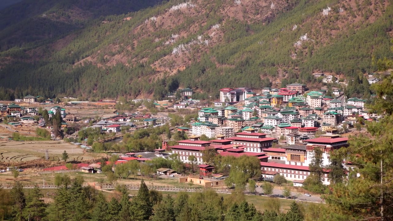 Butan'daki ormanlık dağlarla birlikte Tashichho Dzong ve Thimphu silüetinin geniş açılı panoraması.