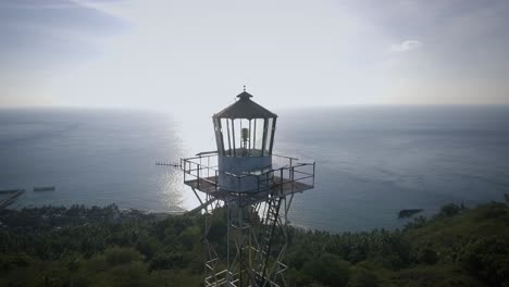 Toma-Aérea-De-Una-Antigua-Torre-De-Acero-De-La-Casa-De-La-Luz-En-Una-Pequeña-Isla,-Respaldada-Por-La-Puesta-De-Sol,-Rodeada-Por-El-Océano-Azul-Por-La-Tarde