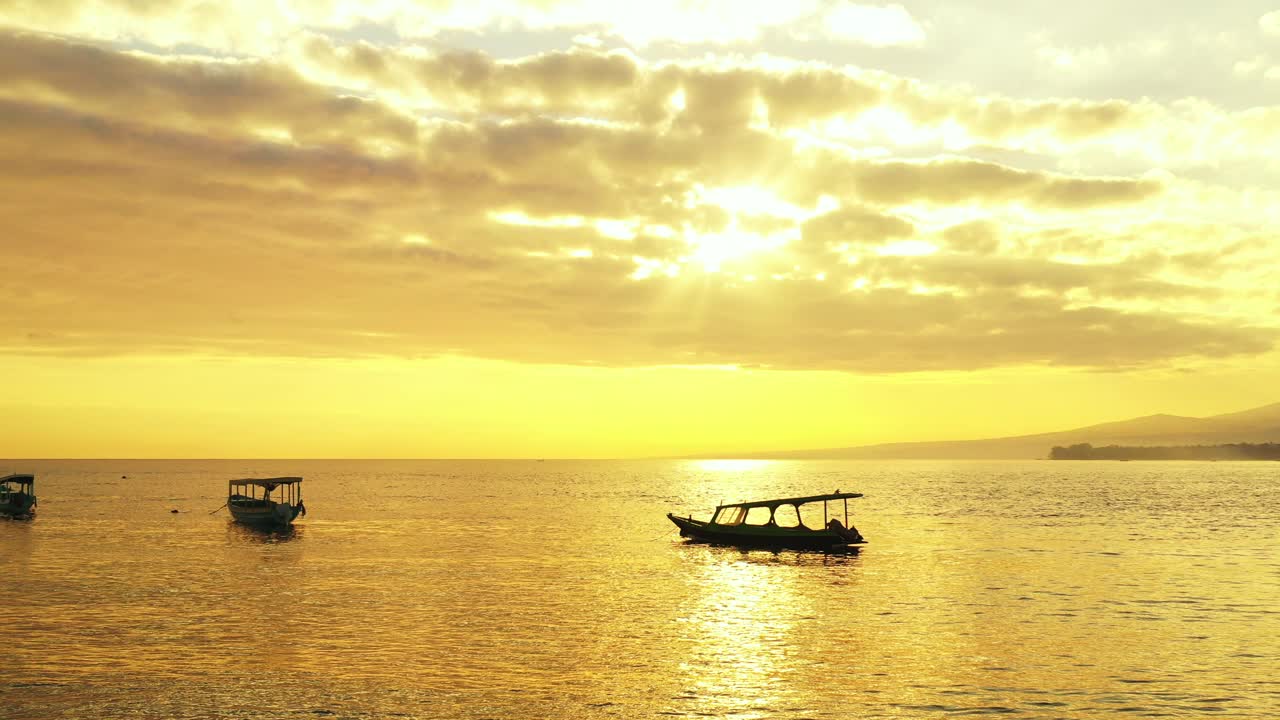 노란 하늘과 태양이 잔잔한 바다 표면에 반사되는 회색 구름을 통해 빛을 비추는 황금빛 바다, 미얀마의 조용한 만에 떠 있는 정박된 보트