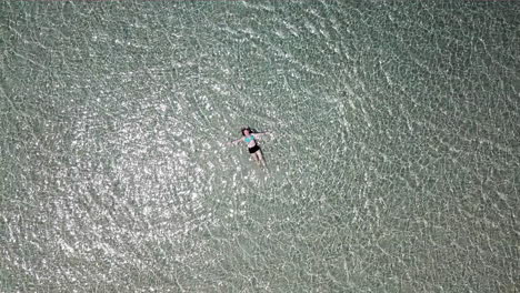 AERIAL LOWERING shot towards a teenage girl lying in shallow water