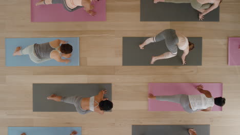 Vista-Superior-Clase-De-Yoga-Mujeres-Sanas-Practicando-Pose-Guerrera-Disfrutando-Del-Estilo-De-Vida-Fitness-Haciendo-Ejercicio-En-El-Gimnasio