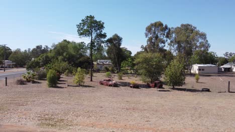 drone taking off revealing rusty old car bodies and a small country town with a highway