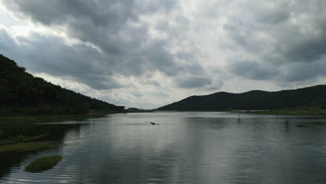 Aerial-footage-on-the-lake-towards-a-gorgeous-scenic-horizon-revealing-rainclouds-reflected-on-water,-quiet-and-a-placid