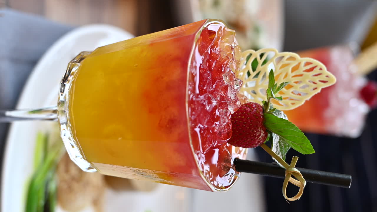Rød og orange cocktail med et jordbær på et bord på en restaurant. Lodret